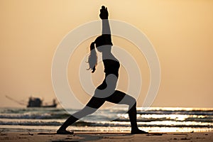 Silhouette Vacation of Asian woman relaxing in yoga Warrior one pose on the sand and beach with sunset beautiful sea in Tropical i