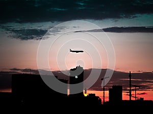 Silhouette view of buildings under a flying airplane with red sunset sky