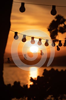 Silhouette of vintage light bulbs on string wire against sunset background