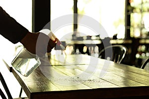 Silhouette waiter cleaning the table with disinfectant spray in a restaurant.