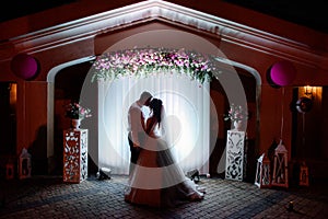 Silhouette of a wedding couple standing before a wall with wedding altar of pik flowers