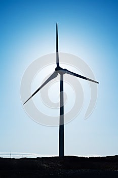 Silhouette of a wind electricity generator against clean blue sky. Warm sunny day. Copy space. Renewable green energy concept