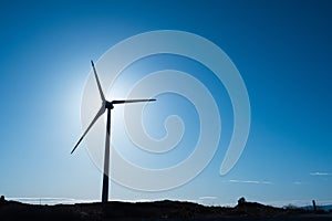 Silhouette of a wind electricity generator against clean blue sky. Warm sunny day. Copy space. Renewable green energy concept