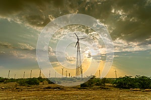 Silhouette of wind mills with a setting sun and cloudy sky in background, Rajasthan, India