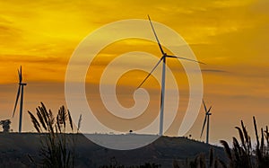 Silhouette wind turbine farm over moutain with orange sunset and