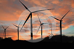 Silhouette of a wind turbine generating electricity on sky sunset background.