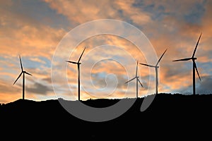 Silhouette of a wind turbine generating electricity on sky sunset background.