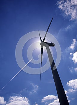 Silhouette of wind turbine with jet aircraft vapour trail photo