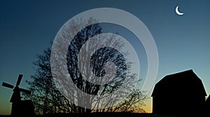 Silhouette of a windmill and barn at twilight.