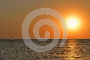 The silhouette of a windsurfer on a board under a sail moves along a calm water surface at sunset over the sea, horizon