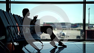 The silhouette of a woman against the light, she is in the waiting room at the airport, throws a backpack on the seat