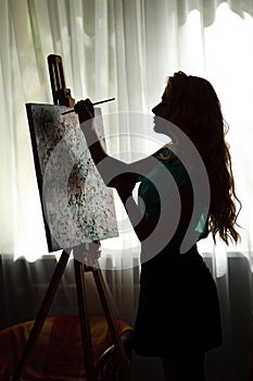 Silhouette woman artist draws paint picture on easel