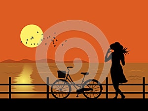 Silhouette of woman and bicycle standing by the sea watching the sunset