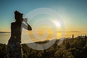 Silhouette of woman with camera. Woman takes photo of La Gomera Island in the rays of the setting sun. Tenerife Island
