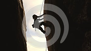 Silhouette of a woman is climbing a rock wall with a rope