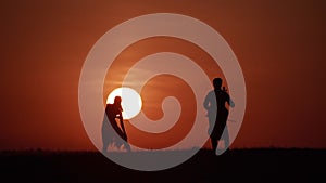 Silhouette of woman dancer and cellist opposite huge sun. Slow motion