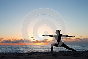 Silhouette of woman doing yoga on the beach at sunrise