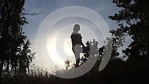 Silhouette of woman doing yoga in evening outdoors background of setting sun.