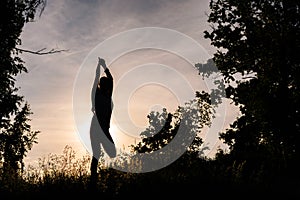 Silhouette of woman doing yoga in evening outdoors background of setting sun.