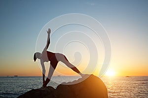 Silhouette of woman doing yoga exercises on the sea coast