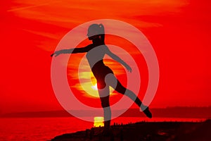 Silhouette of woman doing yoga meditation during sunset with natural golden sunlight on sea