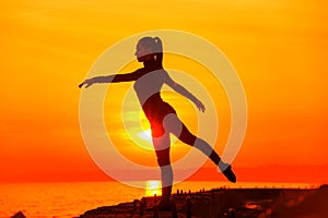 Silhouette of woman doing yoga meditation during sunset with natural golden sunlight on sea