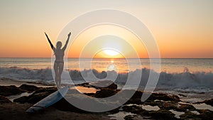 Silhouette of woman. Excited young woman raising arms at the beach in front of the ocean. View from back. Sunset at the beach.