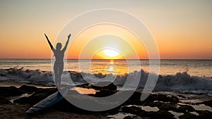 Silhouette of woman. Excited young woman raising arms at the beach in front of the ocean. View from back. Sunset at the beach.