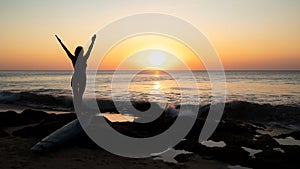 Silhouette of woman. Excited young woman raising arms at the beach in front of the ocean. View from back. Sunset at the beach.