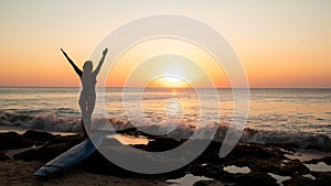 Silhouette of woman. Excited young woman raising arms at the beach in front of the ocean. View from back. Sunset at the beach.