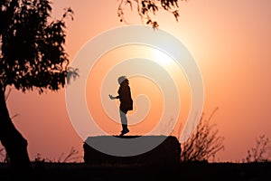 Silhouette of a woman in the field on a straw bale at sunset with the sun behind her and tree branches on her sides
