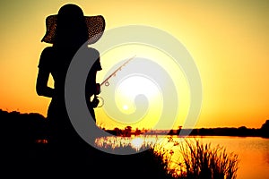 Silhouette of a woman with a fishing rod on the nature at dawn