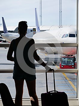 SILHOUETTE: Woman grabs her luggage and looks through the window at airplane.