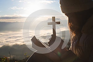 Silhouette of woman hand holding holy lift of christian cross with light sunset background