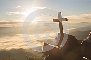 Silhouette of woman hand holding holy lift of christian cross with light sunset background