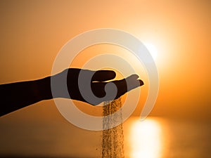 Silhouette of woman hand pouring sand from beach against yellow sky at sunset