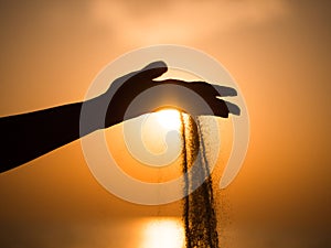 Silhouette of woman hand pouring sand from beach against yellow sky at sunset