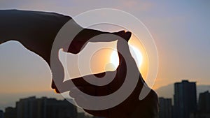 Silhouette of woman hands are doing finger frame against sunset or sunrise sky