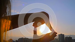 Silhouette of woman hands are doing finger frame against sunset or sunrise sky