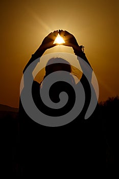 Silhouette of woman hands holding sun in triangle on background