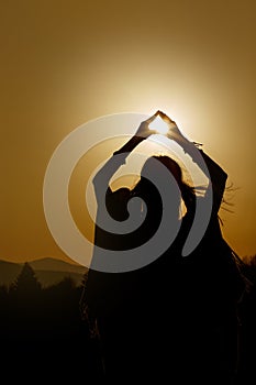 Silhouette of woman hands holding sun in triangle on background