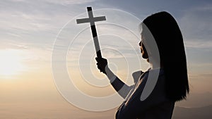 Silhouette of woman hands praying with cross  in nature sunrise background,  Crucifix, Symbol of Faith. Christian life crisis