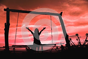 Silhouette of a woman having fun sitting on swing at sundown with beautiful clouds in background,Freedom and happiness for travel