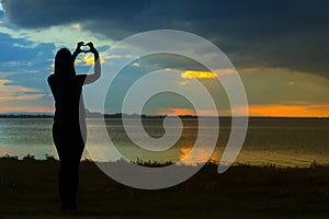 Silhouette of woman with hearth shaped hands on sunset.