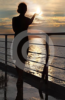 Silhouette of woman holding sun, standing on deck