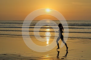 Silhouette of woman jogger running on sunset beach