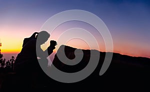 Silhouette of woman kneeling down praying for worship God at sky background. Christians pray to jesus christ for calmness. In