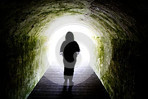 Silhouette of woman in light at end of tunnel