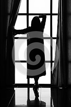 Silhouette of a woman in a long peignoir near a large window