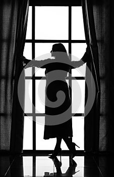 Silhouette of a woman in a long peignoir near a large window